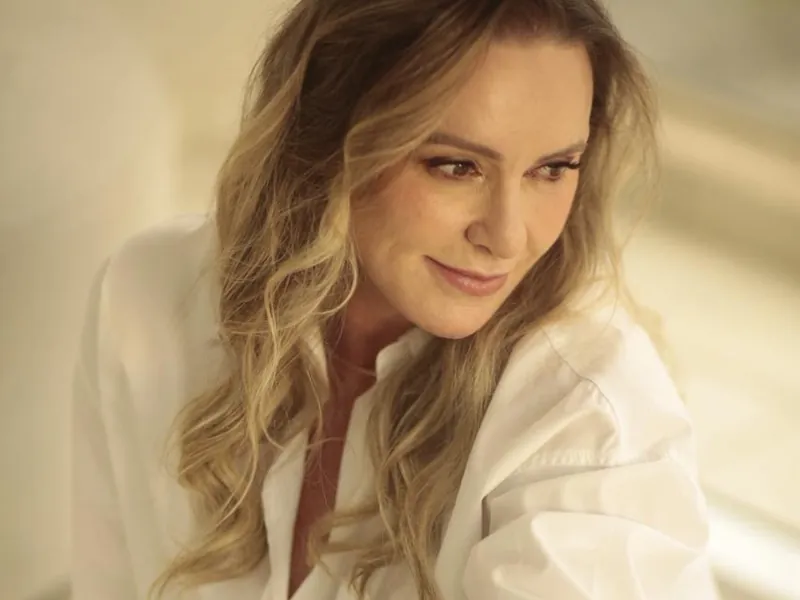 Patrícia Sivieri de camisa branca, sentada, sob luz natural