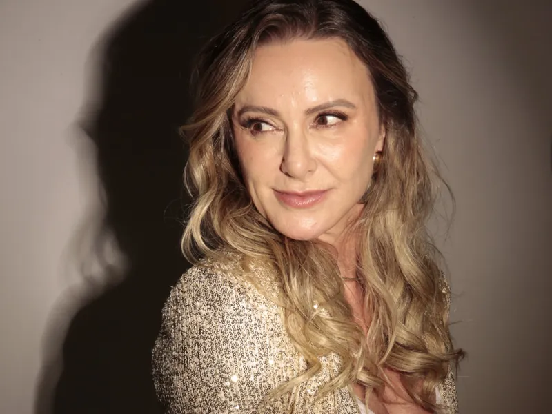 Patrícia Sivieri de blazer dourado, olhando por cima do ombro