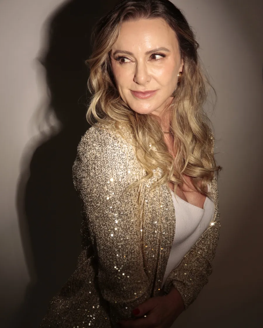 Patrícia Sivieri de blazer dourado, olhando por cima do ombro
